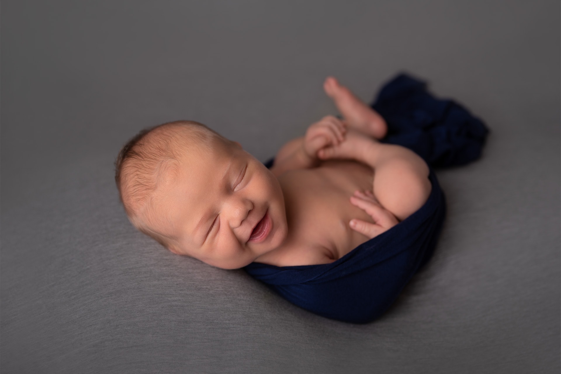 newborn baby boy with big smile posed on gray backdrop in bismarck studio