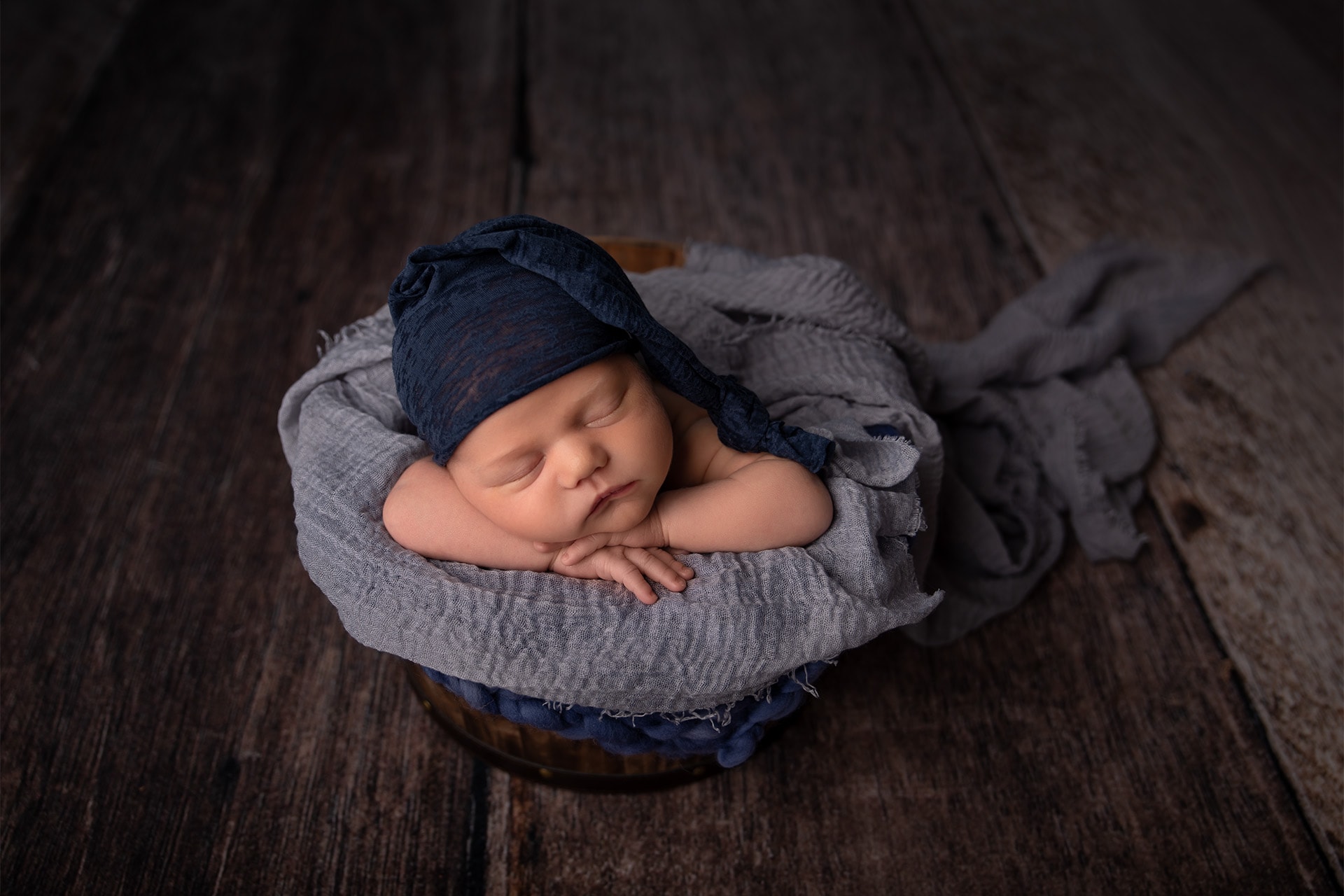 newborn baby boy posed in bucket with blue sleepy hat in bismarck studio