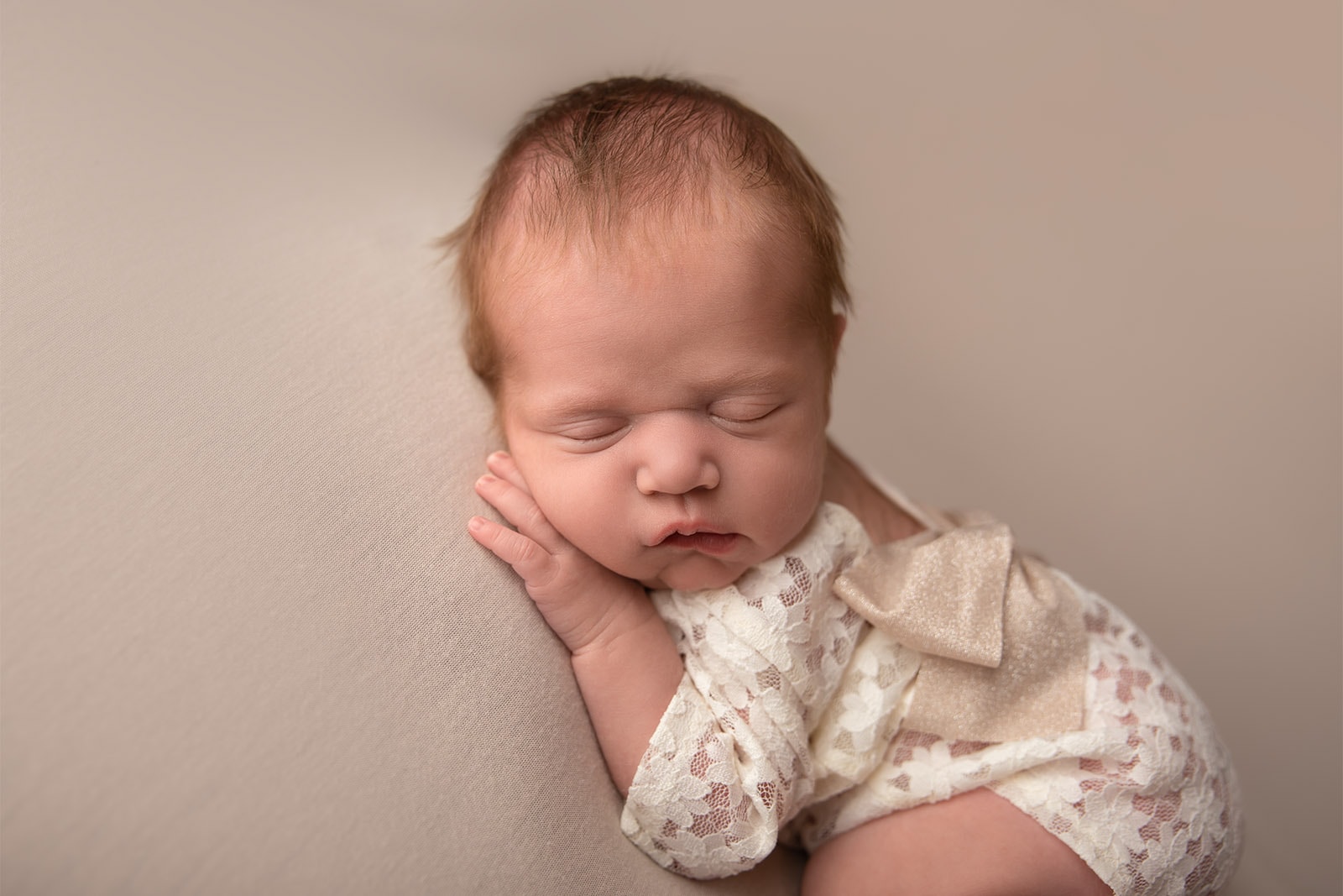 newborn baby girl on cream wearing lace romper
